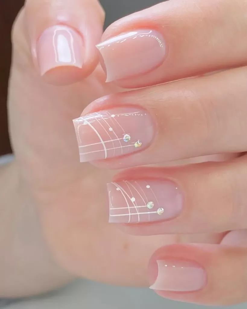 Unhas decoradas com francesinha artística em linhas brancas finas e pedrarias delicadas, estilo elegante e moderno.