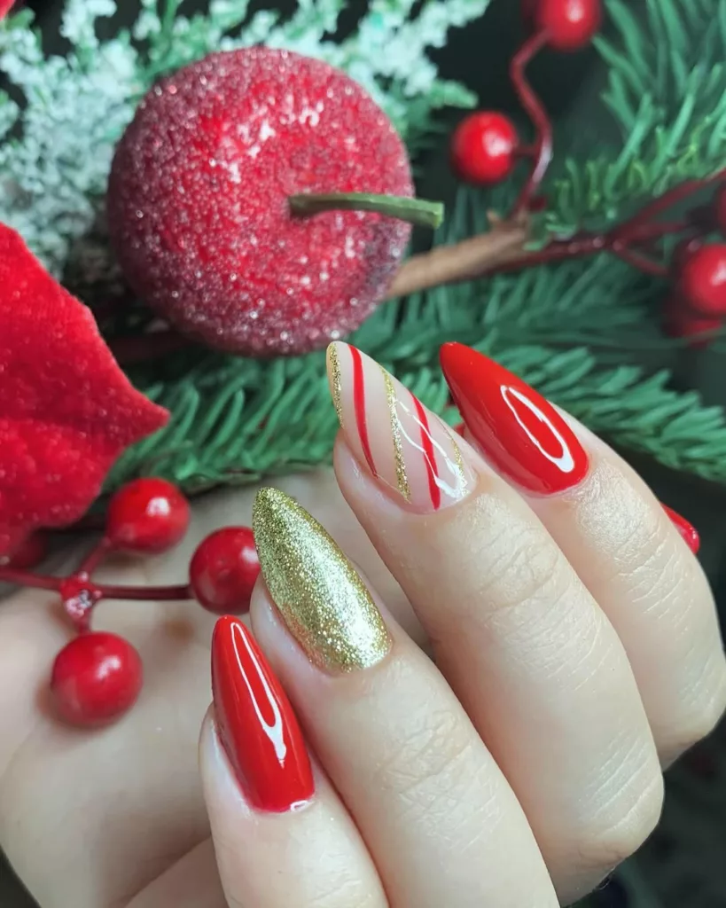 Unhas natalinas com esmalte vermelho intenso, glitter dourado e design de listras em branco e vermelho com detalhe dourado, lembrando bala de menta natalina.