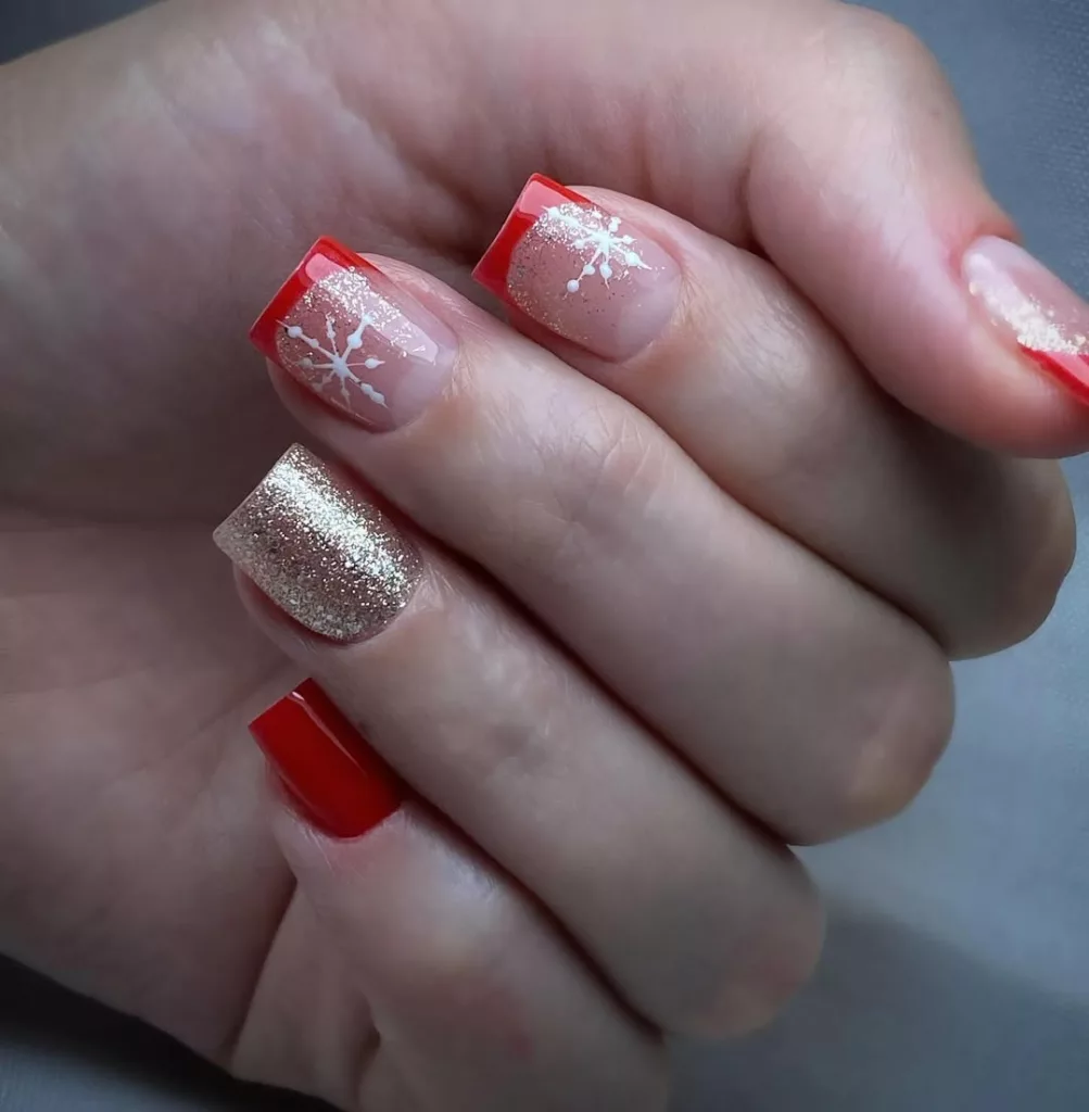 Unhas decoradas com francesinha vermelha, flocos de neve brancos e glitter dourado, remetendo a uma estética natalina invernal e delicada.