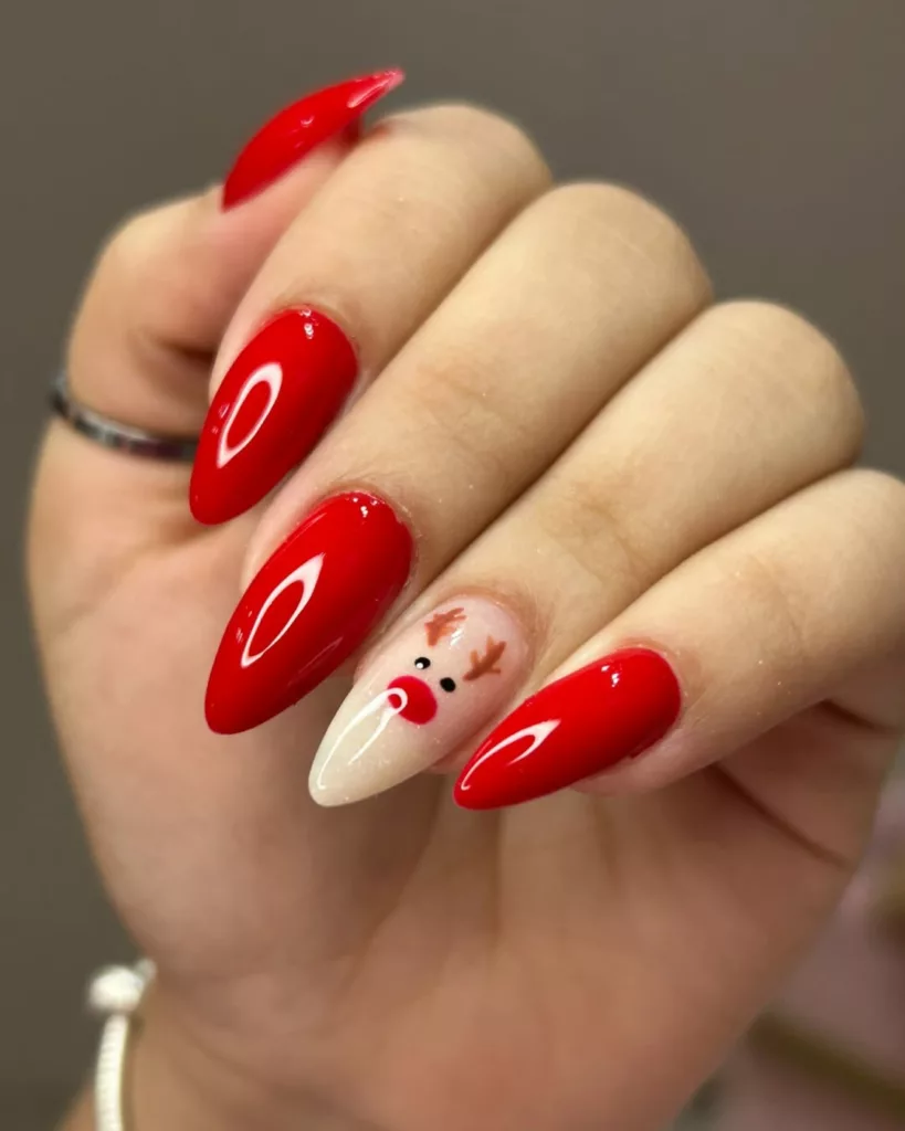 Unhas de Natal vermelhas com brilho intenso e uma unha decorada com desenho de rena natalina.