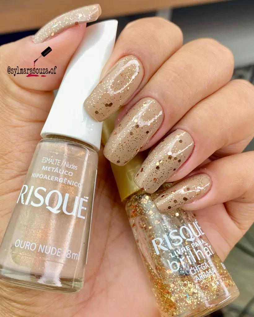 Unhas nude metálicas com partículas de glitter dourado espalhadas, formando um visual moderno e festivo ideal para o Réveillon.