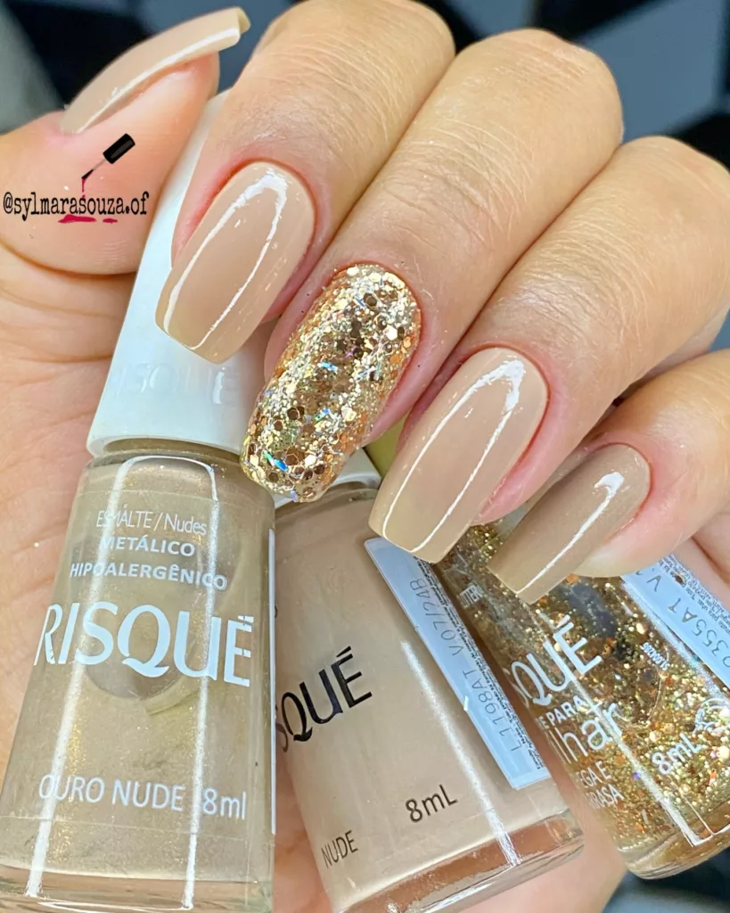 Unhas nude clássicas com uma unha filha única em glitter dourado intenso, proposta minimalista e elegante para a virada do ano.