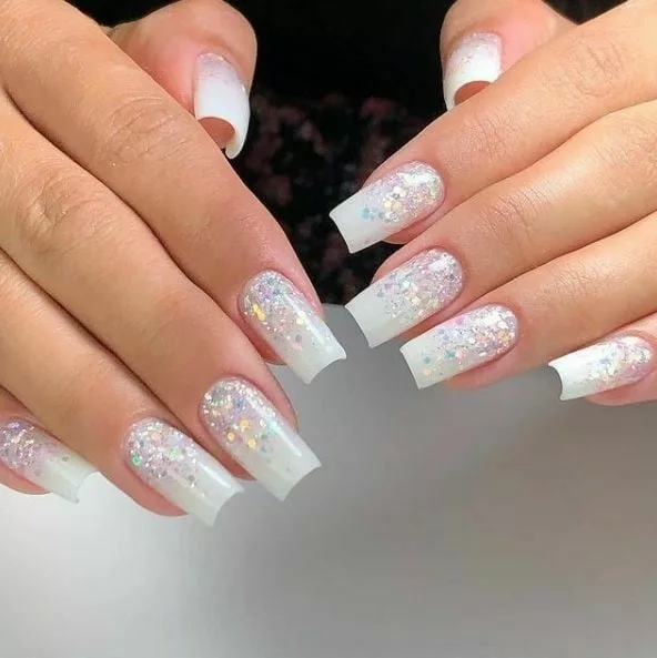 Unhas quadradas com base branca e degradê de glitter iridescente, criando um efeito brilhante e sofisticado para o Ano Novo.