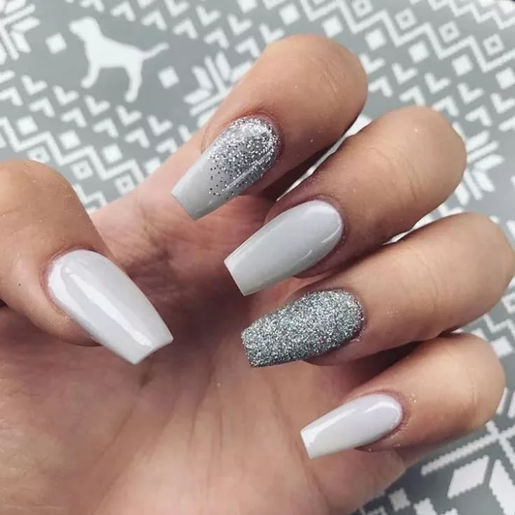 Unhas quadradas em tom branco gelo com um dedo prateado em glitter, formando uma composição sofisticada e moderna para o Ano Novo.